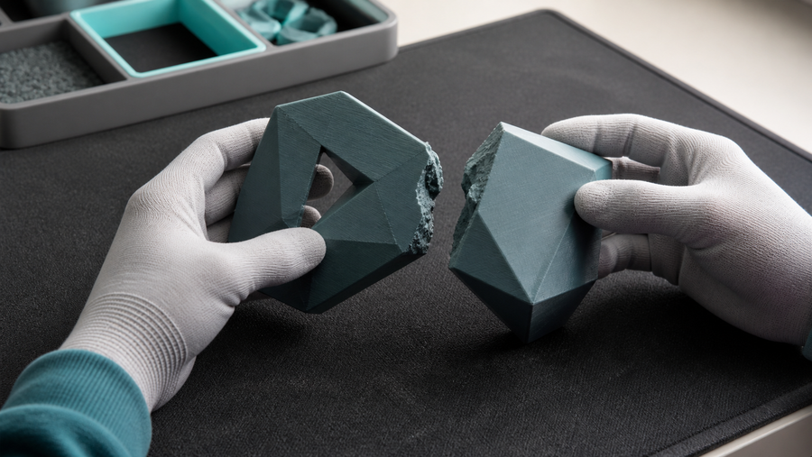 Gloved hands assessing two broken pieces of an abstract 3D printed test sculpture